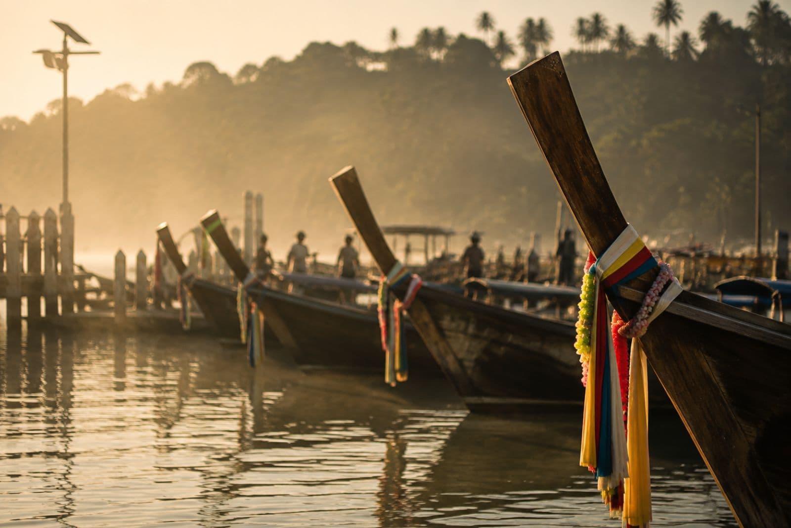 Longtail boats at a dock adorned with garlands in morning mist